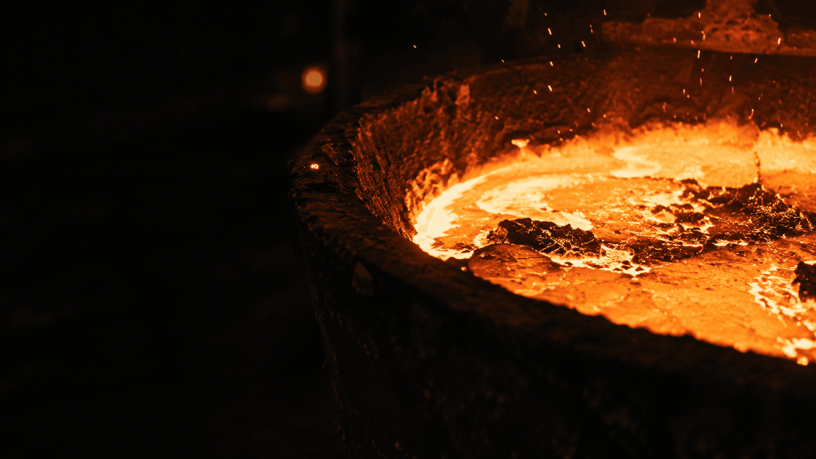 Molten steel in a ladle, the surface breaking bright orange inside a dark refractory shell.