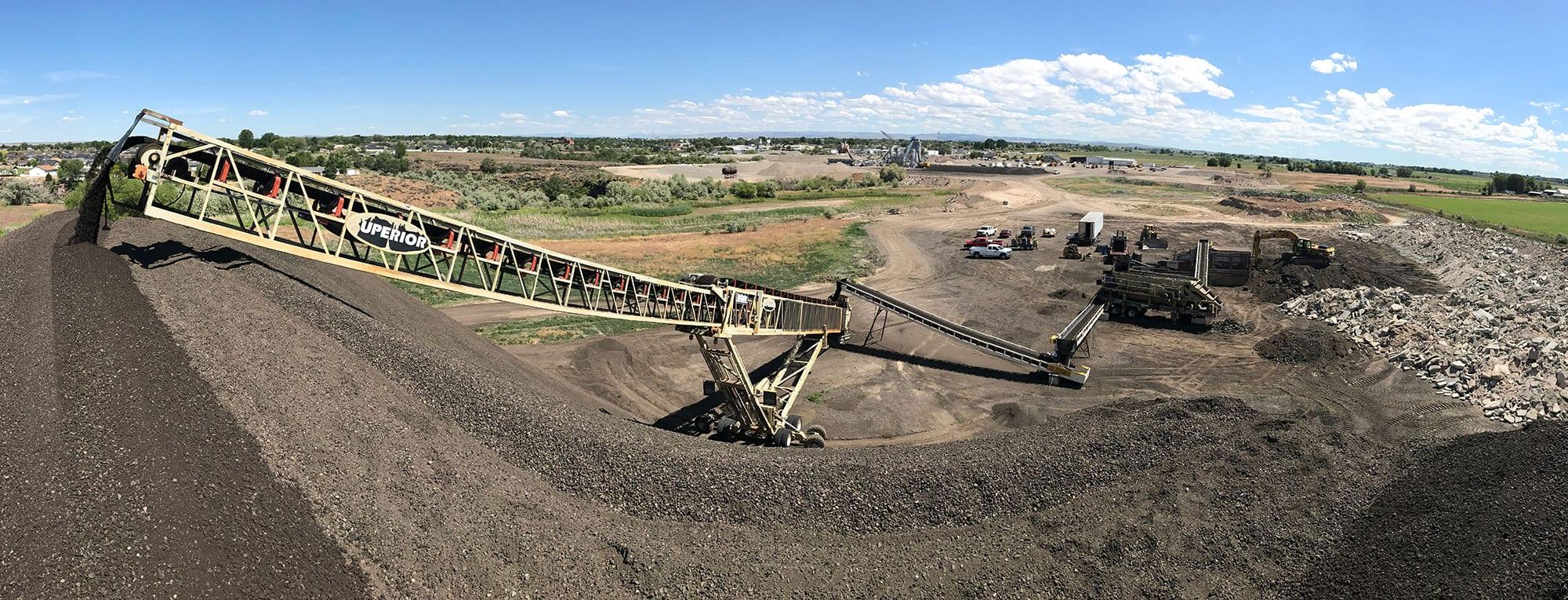 An aggregate plant in summer: a stacker discharging onto a stockpile, crushing and screening plant beyond.