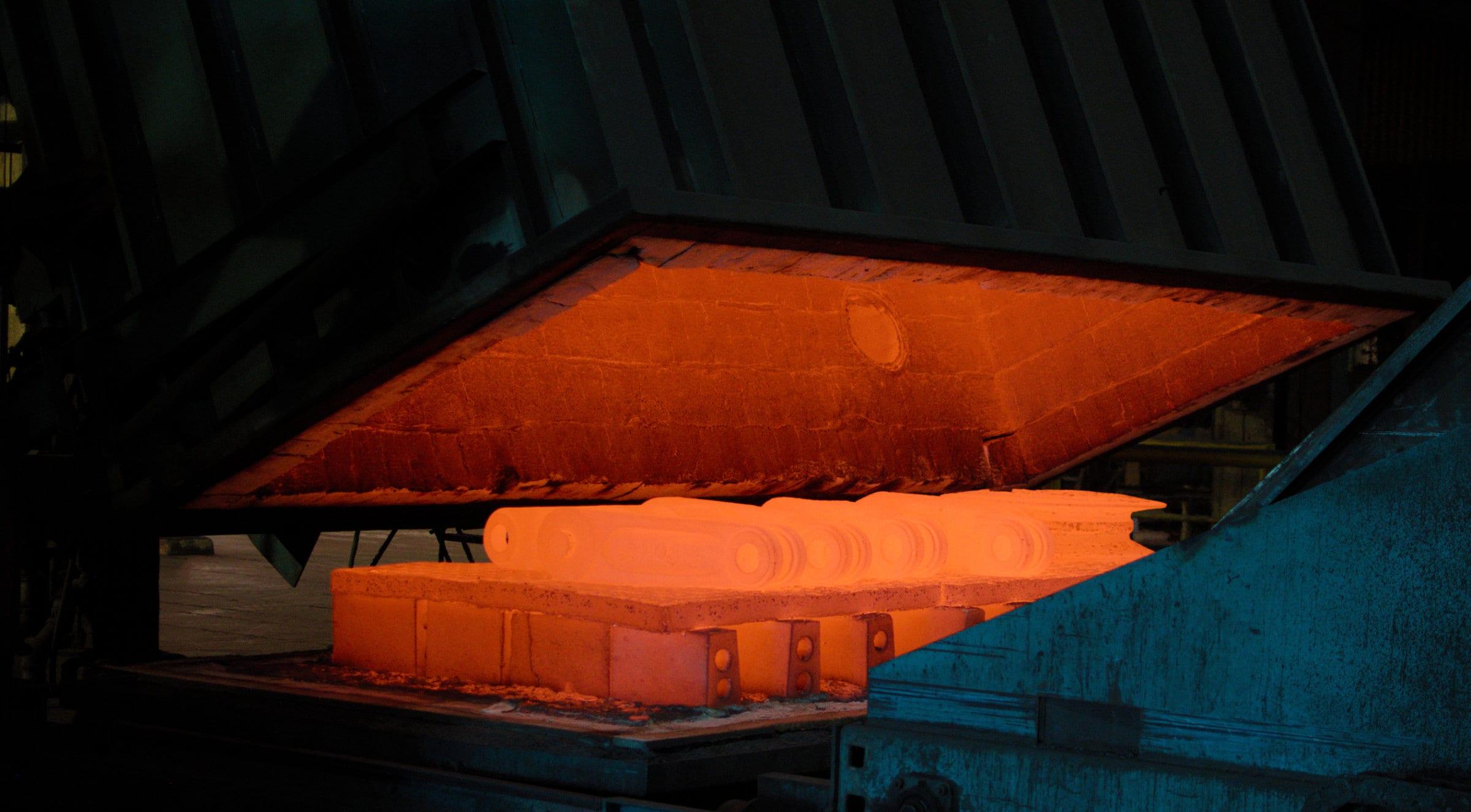 The heat treat furnace with its door raised, a load of castings glowing orange on the hearth inside.