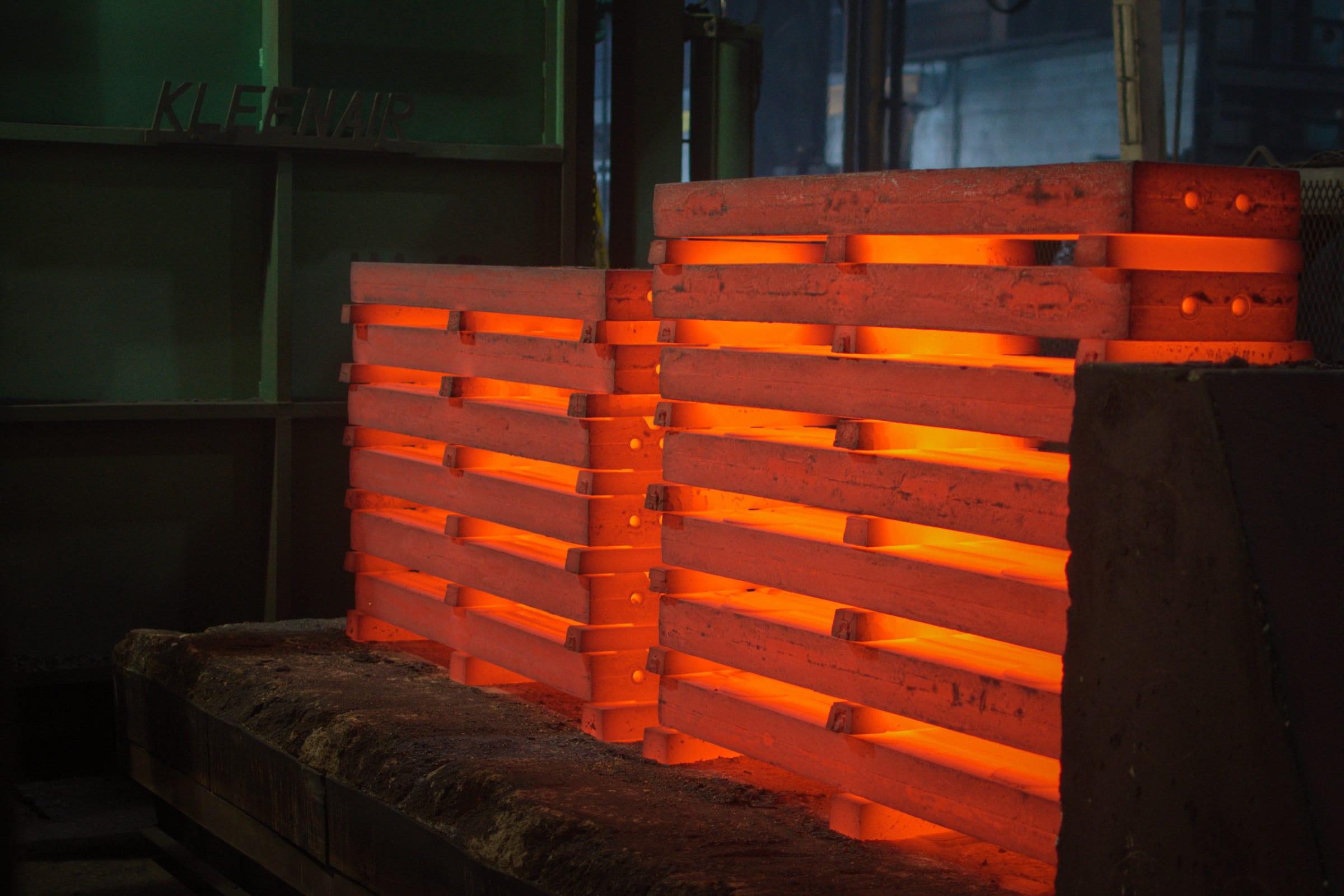 Two stacks of castings glowing orange on the heat treat deck, cooling in open air.