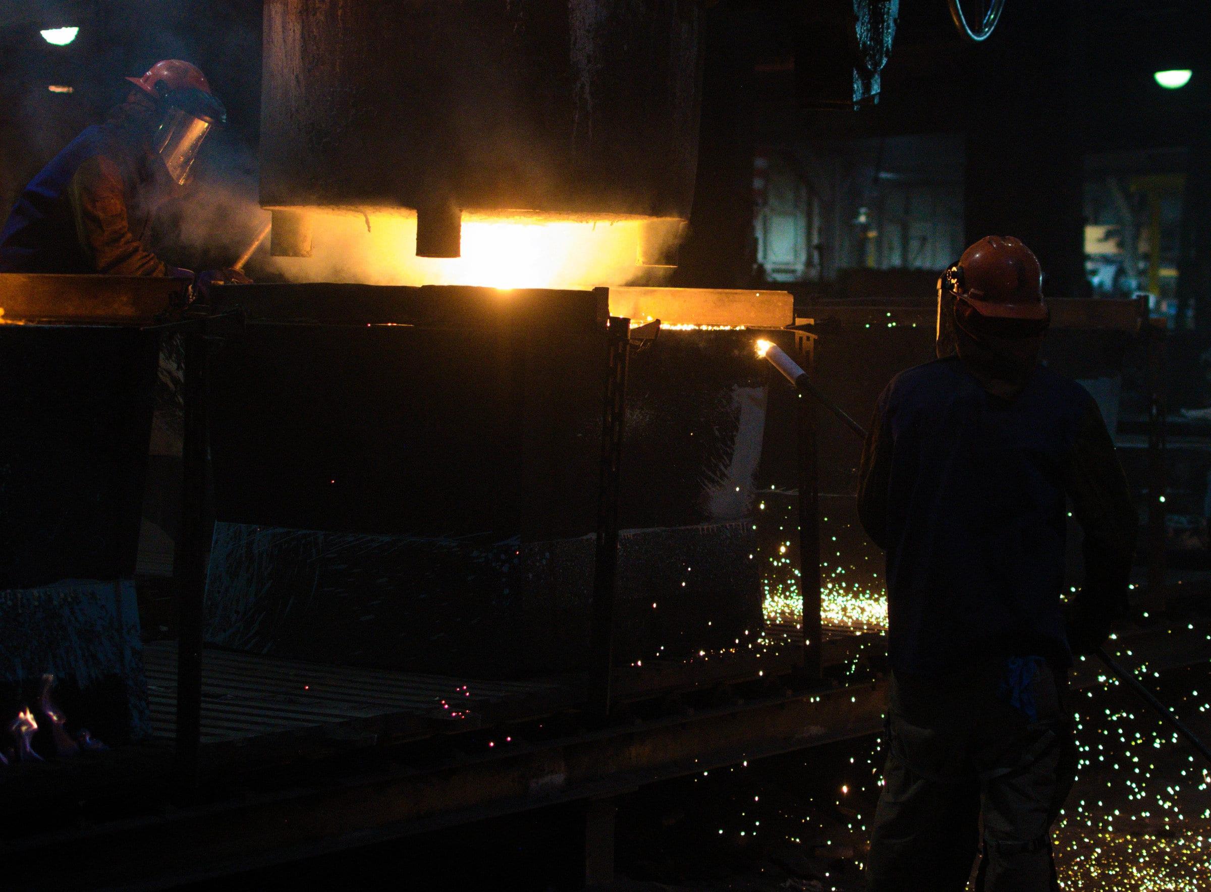 The pouring floor: a ladle held over the molds, sparks crossing the frame, crews working either side.