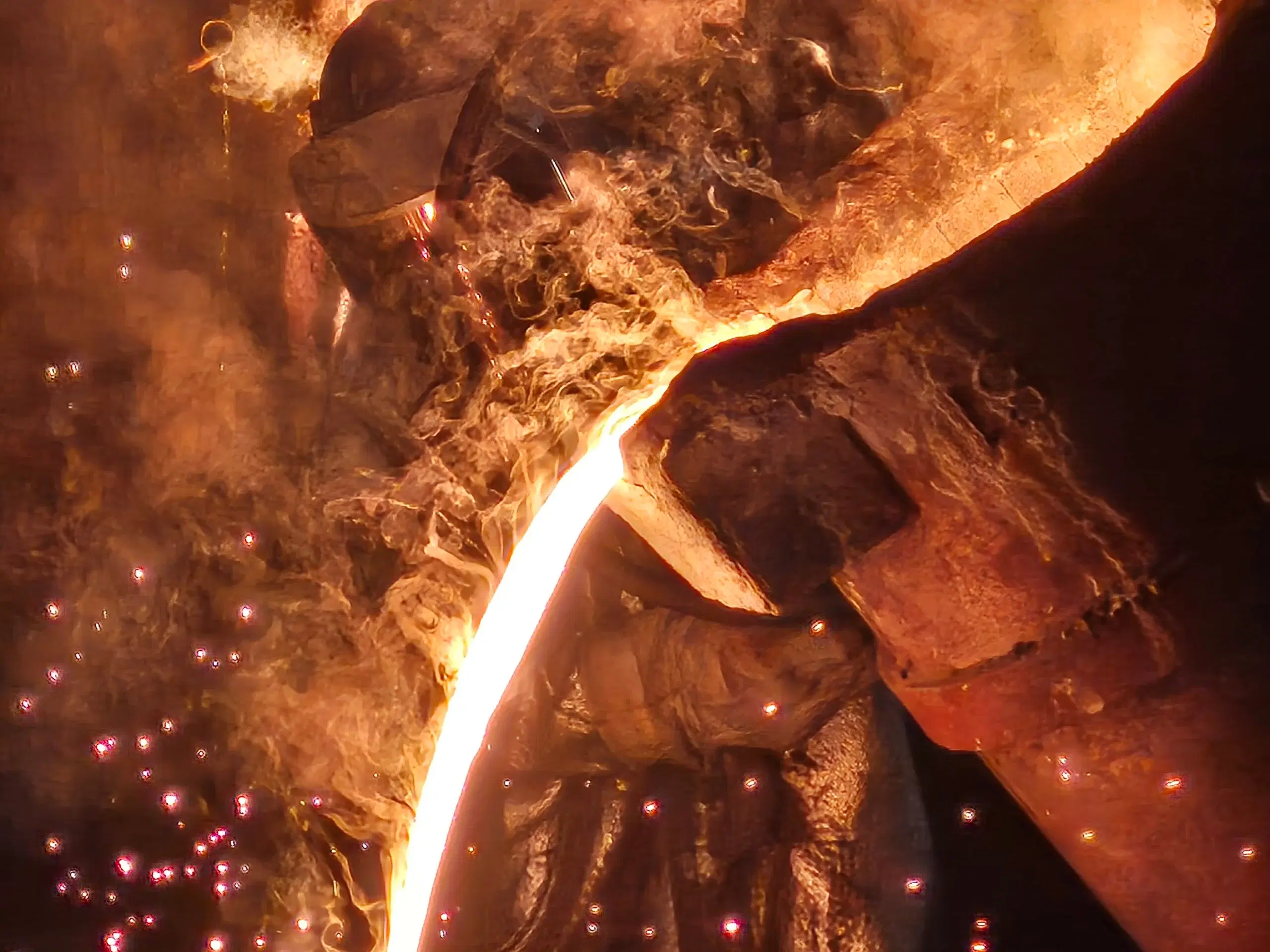 A stream of molten metal running from the spout, close enough to read the turbulence on its surface.