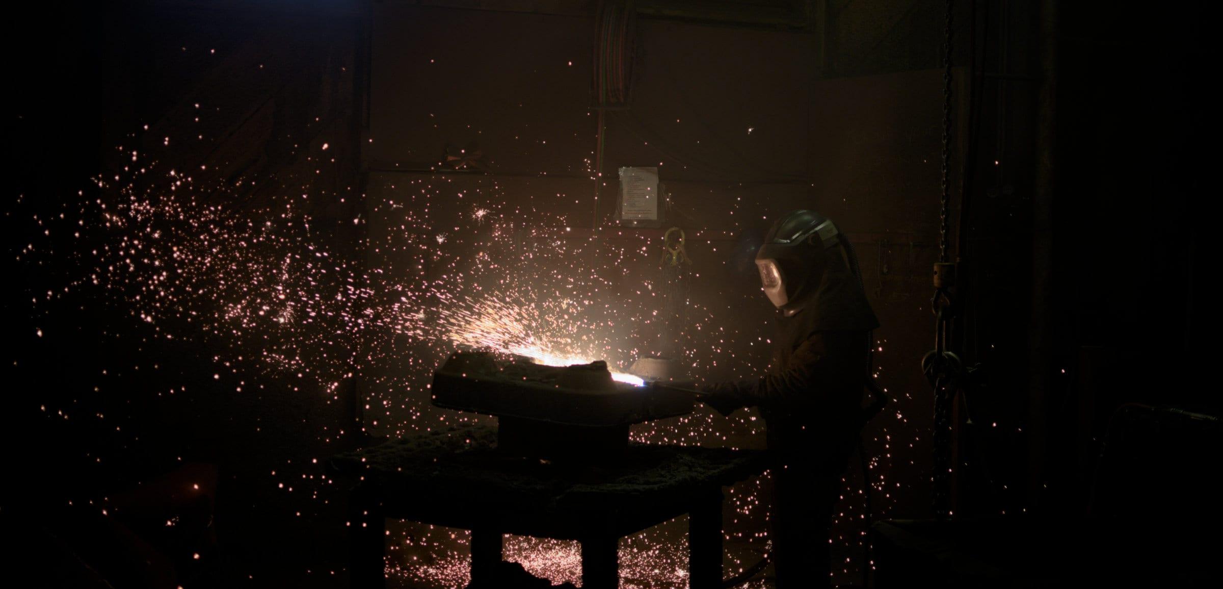 A worker cutting gating off a casting with a torch, a wide fan of sparks across the frame.